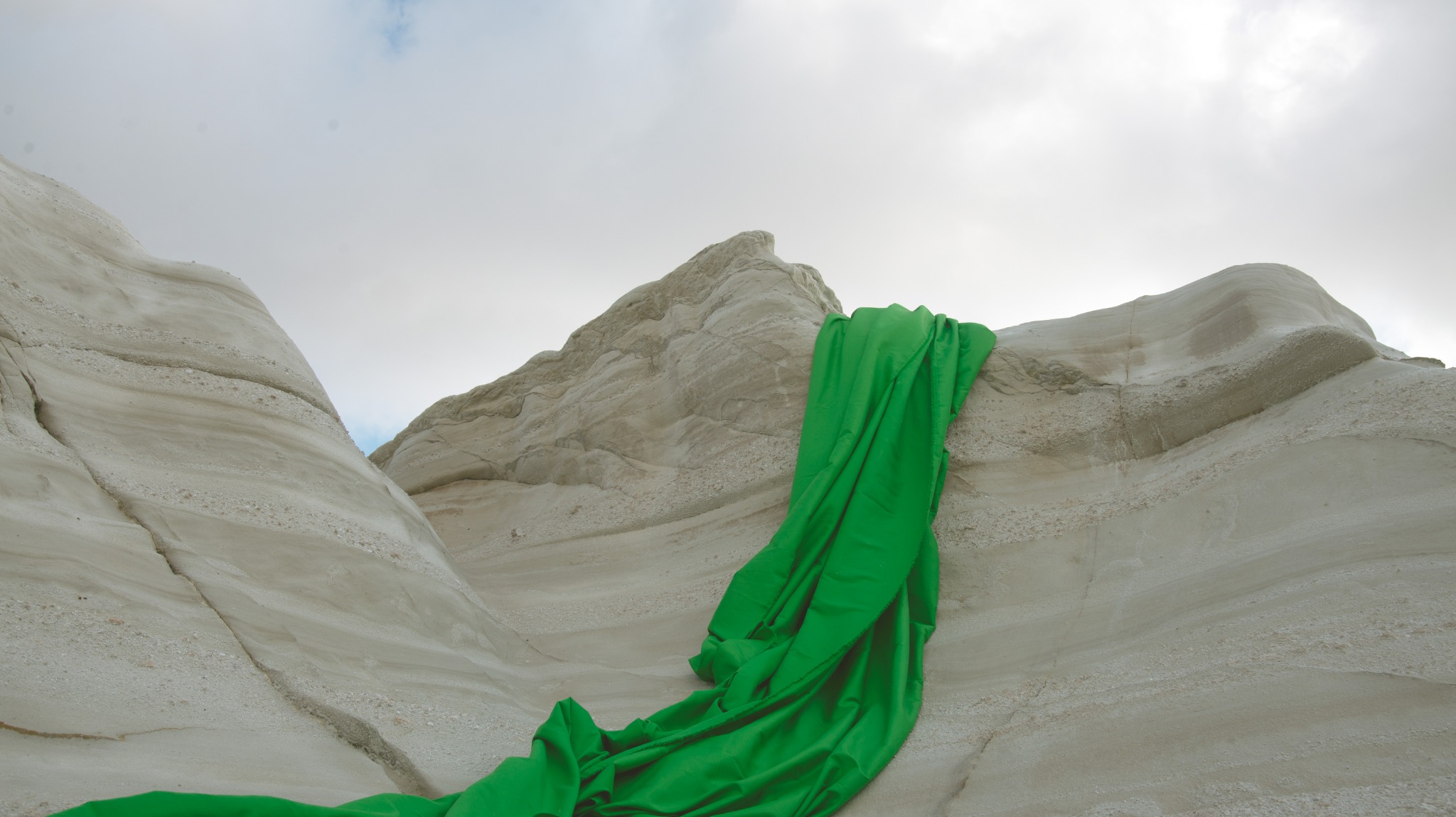 Green-screen fabric falling over the white rock formations of Sarakiniko